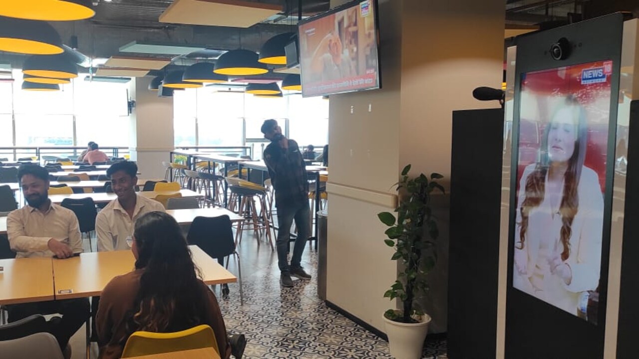 Through the screen News18 anchors - Zakka Jacob, managing editor, News18, Rahul Shivshankar, consulting editor, Network18 and Rubika Liyaquat, consulting editor, News18 India interact with people who sit around or pass by the screen in the GroupM office.